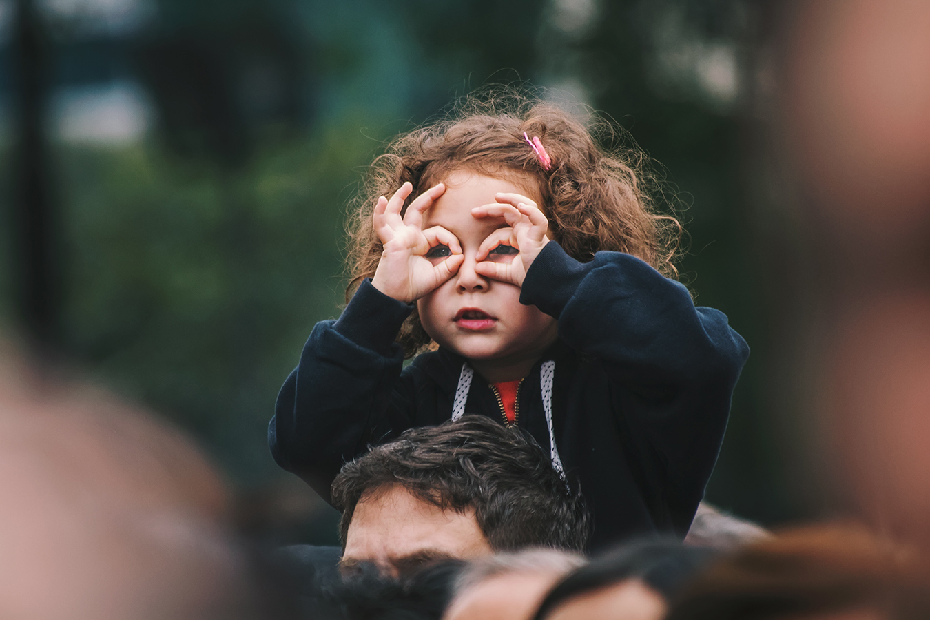 child on parent's shoulders with fingers shaped like glasses